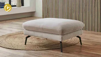 Moderner Hocker in hellem Stoffbezug mit schwarzen Metallfüßen – Teil einer Design-Sitzgruppe in einem stilvollen Wohnzimmer mit Holzlamellenwand, Holzboden und rundem Juteteppich, der Wärme und Natürlichkeit ausstrahlt.